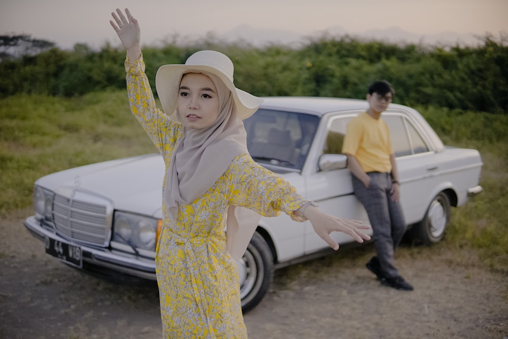 a woman in a yellow dress standing next to a white car