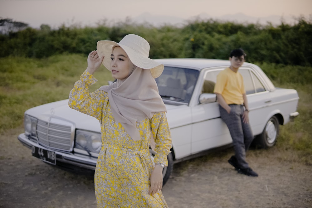 a woman in a yellow dress standing next to a white car