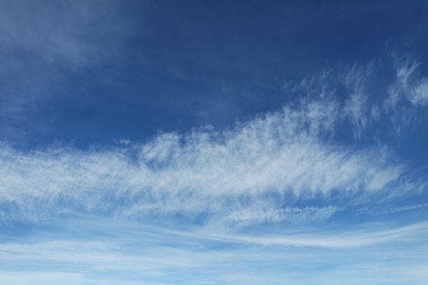 A serene expanse of pale blue sky with gentle, wispy clouds spreading across the horizon.