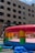 A colorful inflatable bounce house is set up on a city street, surrounded by bubbles floating in the air. Children are playing inside, and a few adults are nearby. The scene is in front of a multi-story building with many windows.