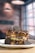 A decadent dessert is served on a white plate, featuring layers of waffles topped with a generous amount of creamy chocolate sauce, drizzles of syrup, and garnished with chocolate sandwich cookies.
