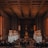 A grand, dimly lit banquet hall with high ceilings and ornate metalwork. Large statues flank a central walkway leading to a prominent statue at the far end. The room is filled with dining tables and chairs, giving an impression of elegance and formality.