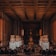 A grand, dimly lit banquet hall with high ceilings and ornate metalwork. Large statues flank a central walkway leading to a prominent statue at the far end. The room is filled with dining tables and chairs, giving an impression of elegance and formality.