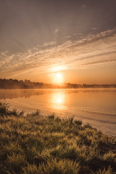 A serene landscape showing a fleeting sunset over a quiet lake, highlighting natural light and reflections.