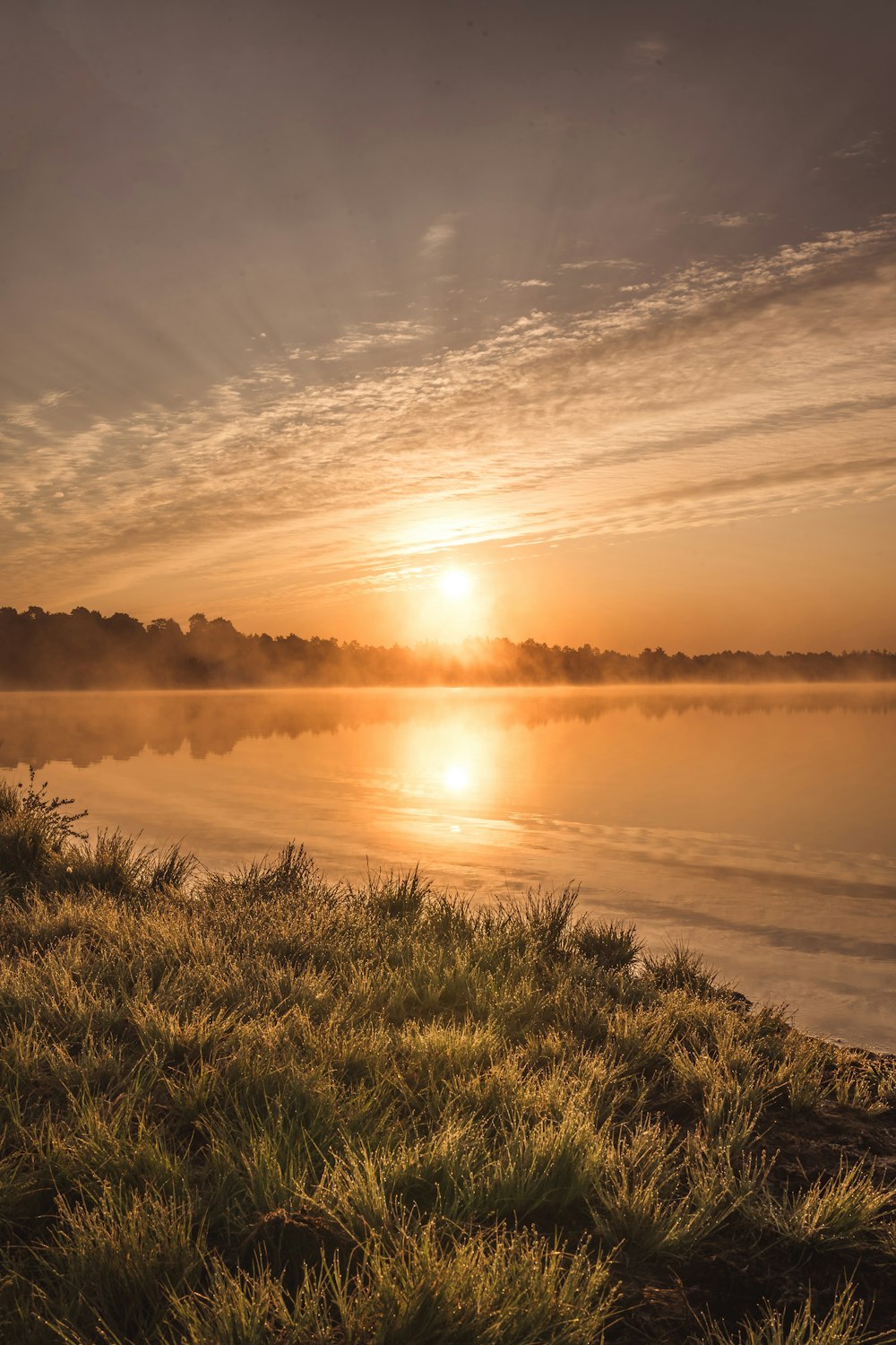 the sun is setting over the water on a foggy day