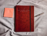 A red and black branded notebook with financial notes and a pen.