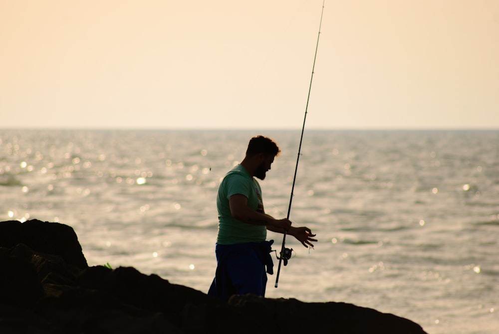 A man standing on a beach holding a fishing pole photo – Free Water Image  on Unsplash