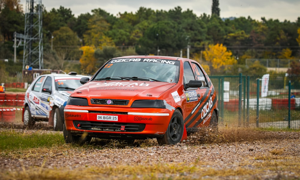 a red car driving down a dirt road next to another car