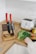A small kitchen counter with wooden surfaces featuring a knife block with two knives that have red handles. Nearby, there is a person’s hand cutting fresh herbs and vegetables on a cutting board. A white toaster and a jar of spices are also present on the counter.