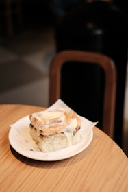 An inviting image of a rustic cinnamon roll with icing on a ceramic plate.