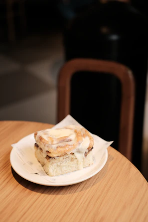 Close-up of a soft cinnamon roll with cream cheese icing on a rustic wooden board.