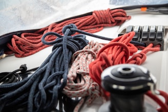 An assortment of ropes, including red, black, and patterned ones, are neatly coiled and arranged on a white surface. In the background, there are some mechanical levers or switches positioned next to the ropes.