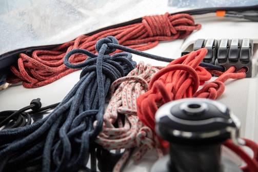 An assortment of ropes, including red, black, and patterned ones, are neatly coiled and arranged on a white surface. In the background, there are some mechanical levers or switches positioned next to the ropes.
