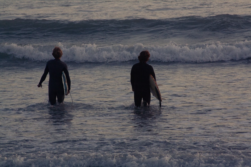 a couple of men standing in the ocean holding surfboards