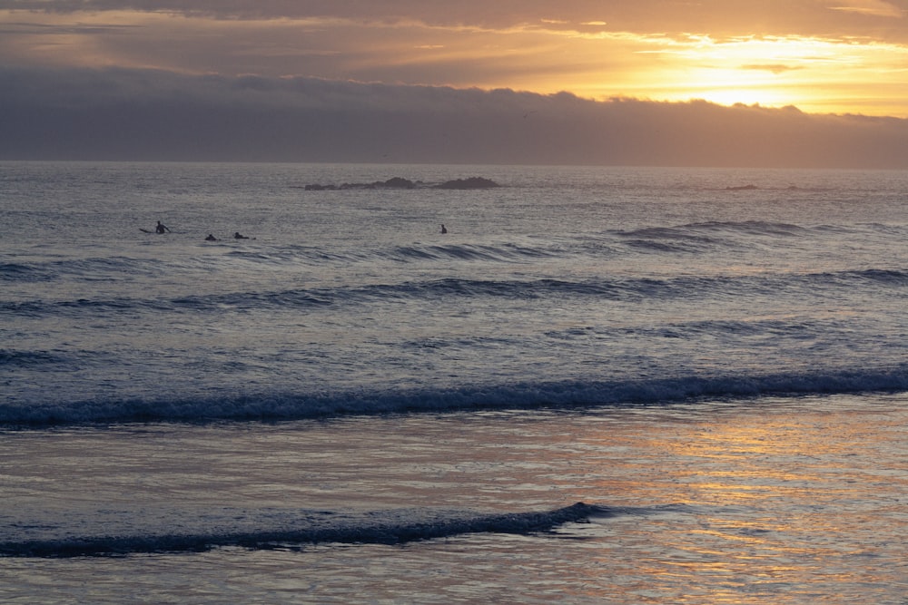 the sun is setting over the ocean with surfers in the water