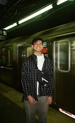 A smiling traveler holding a train ticket while standing on a bustling platform.