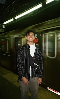 A smiling traveler holding a train ticket while standing on a bustling platform.