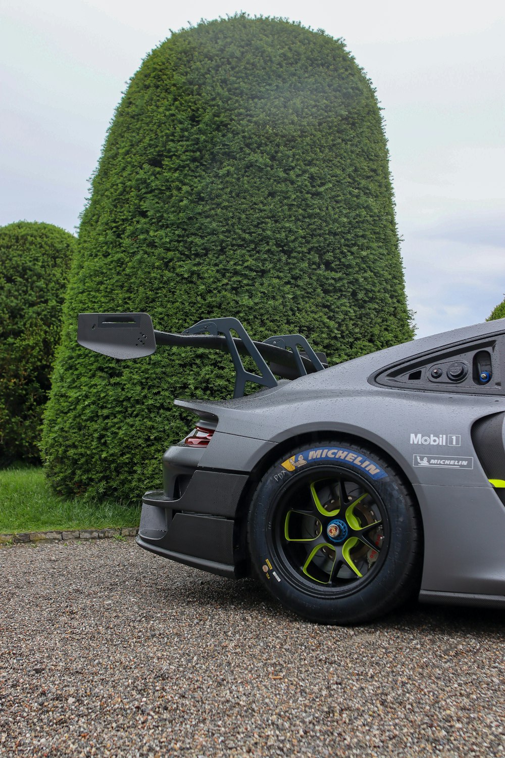 a silver sports car parked in front of a green hedge