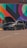 A dark gray car with its hood open is parked in front of a vibrant mural featuring geometric shapes and a variety of colors including red, orange, blue, and green. Two people are standing nearby, possibly inspecting or discussing the car.