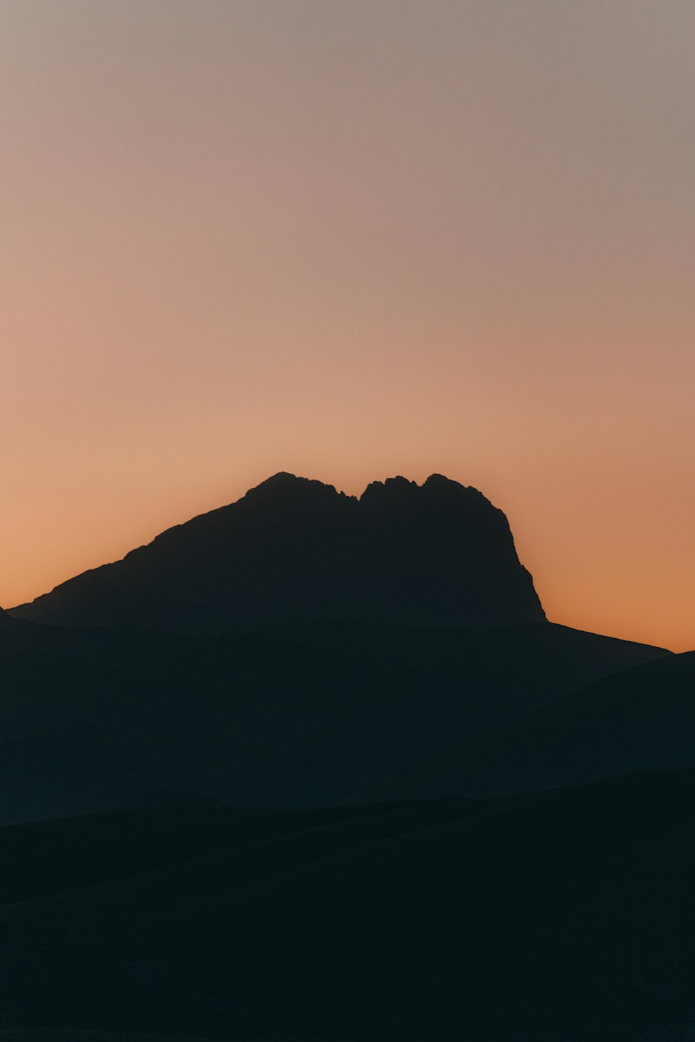 the silhouette of a mountain against a sunset sky