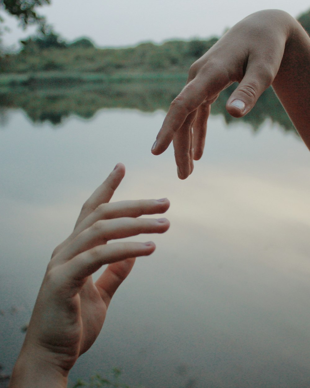 two hands reaching out towards each other over a body of water