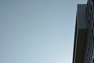 A minimalistic shot of a modern building's facade with clean lines and a geometric pattern against a clear, pale blue sky. The image emphasizes the building's architectural features with a focus on its sleek design.