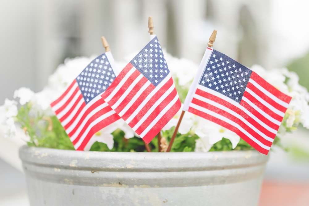 three american flags are placed in a pot of flowers