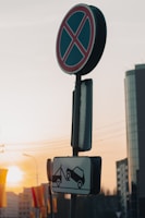A 'no parking' sign with a towing warning depicted below, positioned against a backdrop of a modern cityscape at sunset. The sky has warm hues, and the sun casts a soft glow on the buildings.