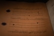 An ancient manuscript featuring Arabic calligraphy written in dark ink on aged, yellow-brown paper. Decorative circular emblems are present alongside the text, adding an ornamental touch.