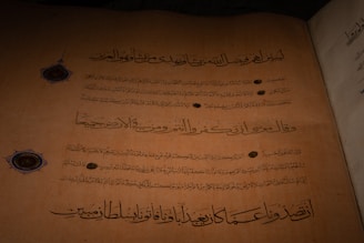 An ancient manuscript featuring Arabic calligraphy written in dark ink on aged, yellow-brown paper. Decorative circular emblems are present alongside the text, adding an ornamental touch.