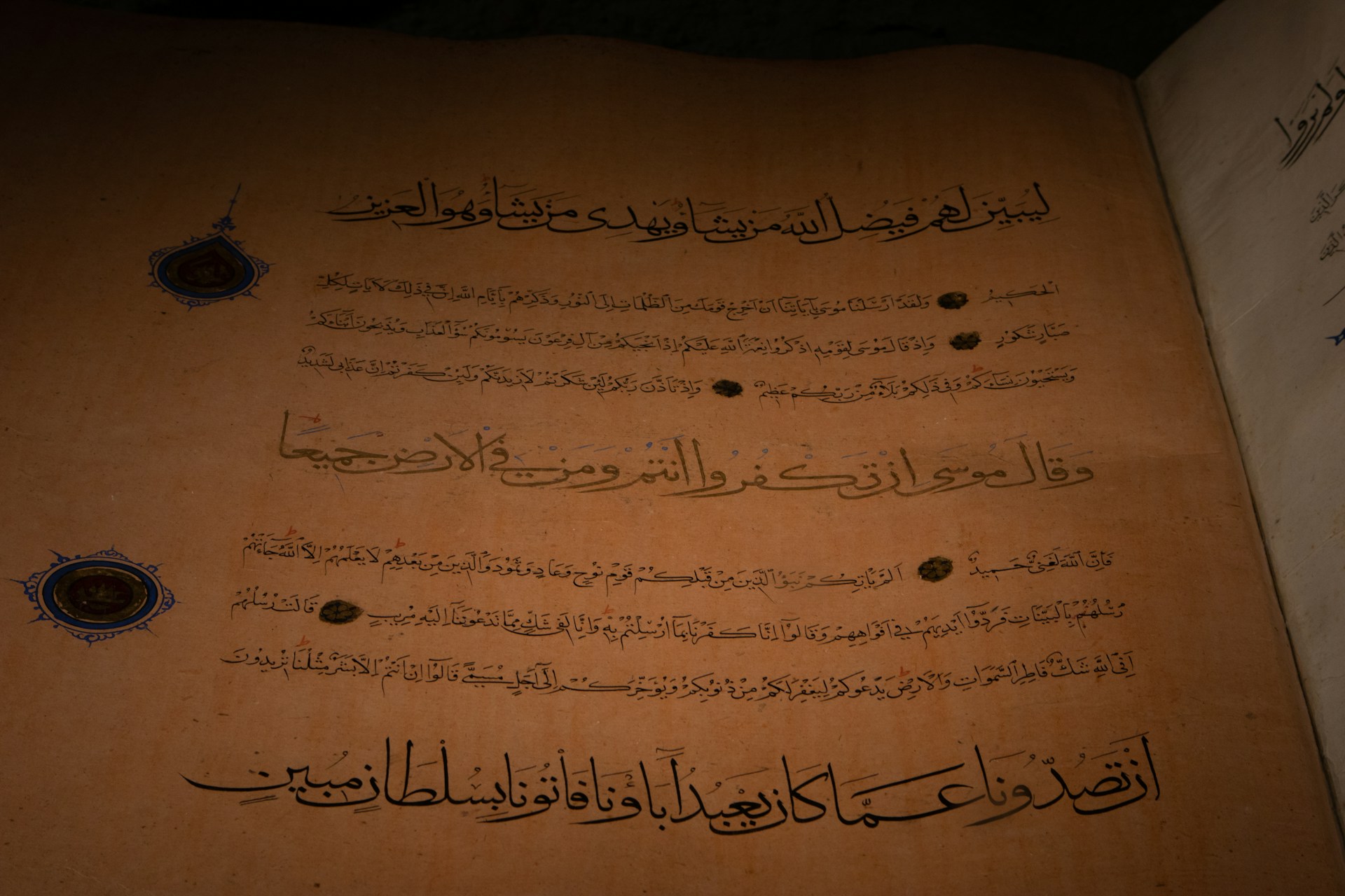 An ancient manuscript featuring Arabic calligraphy written in dark ink on aged, yellow-brown paper. Decorative circular emblems are present alongside the text, adding an ornamental touch.
