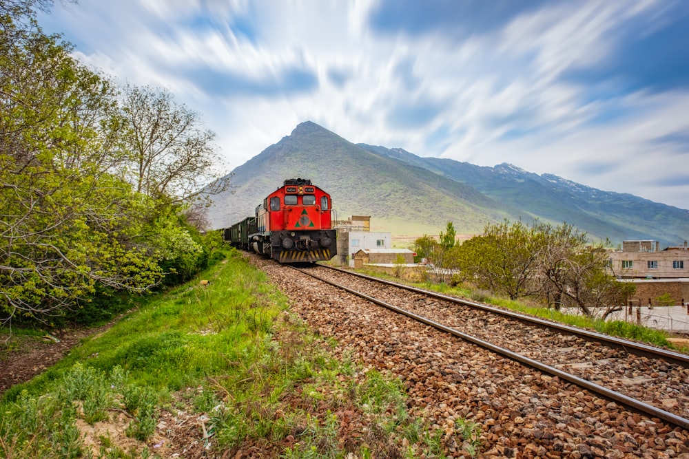 a red train traveling down train tracks next to a lush green hillside