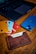 A close-up of a wooden table with a leather cardholder containing several bank cards, each in different colors. A smartphone with a blue case and an Apple logo is positioned next to a laptop with a dark keyboard, partially visible in the background.