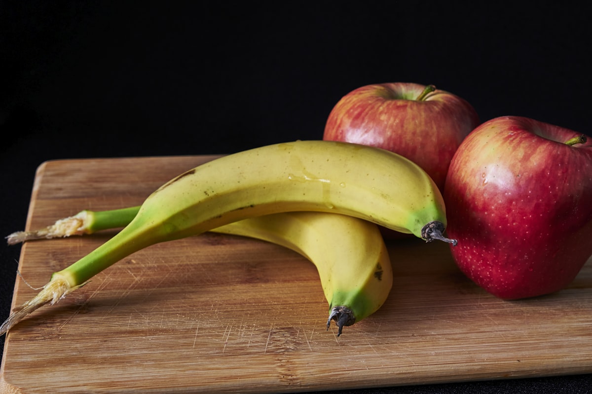 나무 도마 위에 올려진 사과 두 개와 바나나 두 개