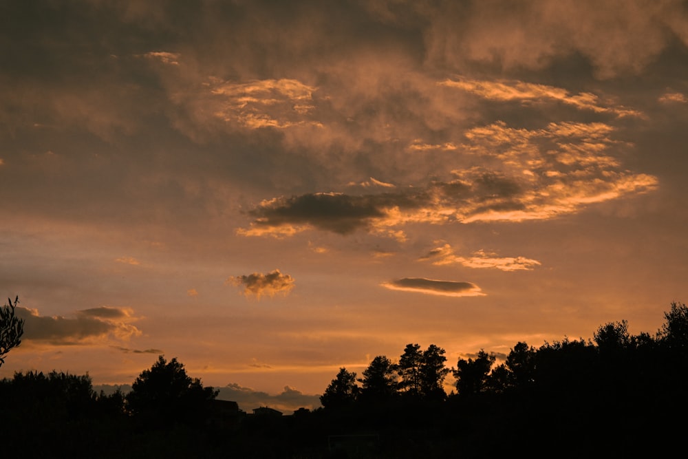 a sunset with clouds and trees in the foreground