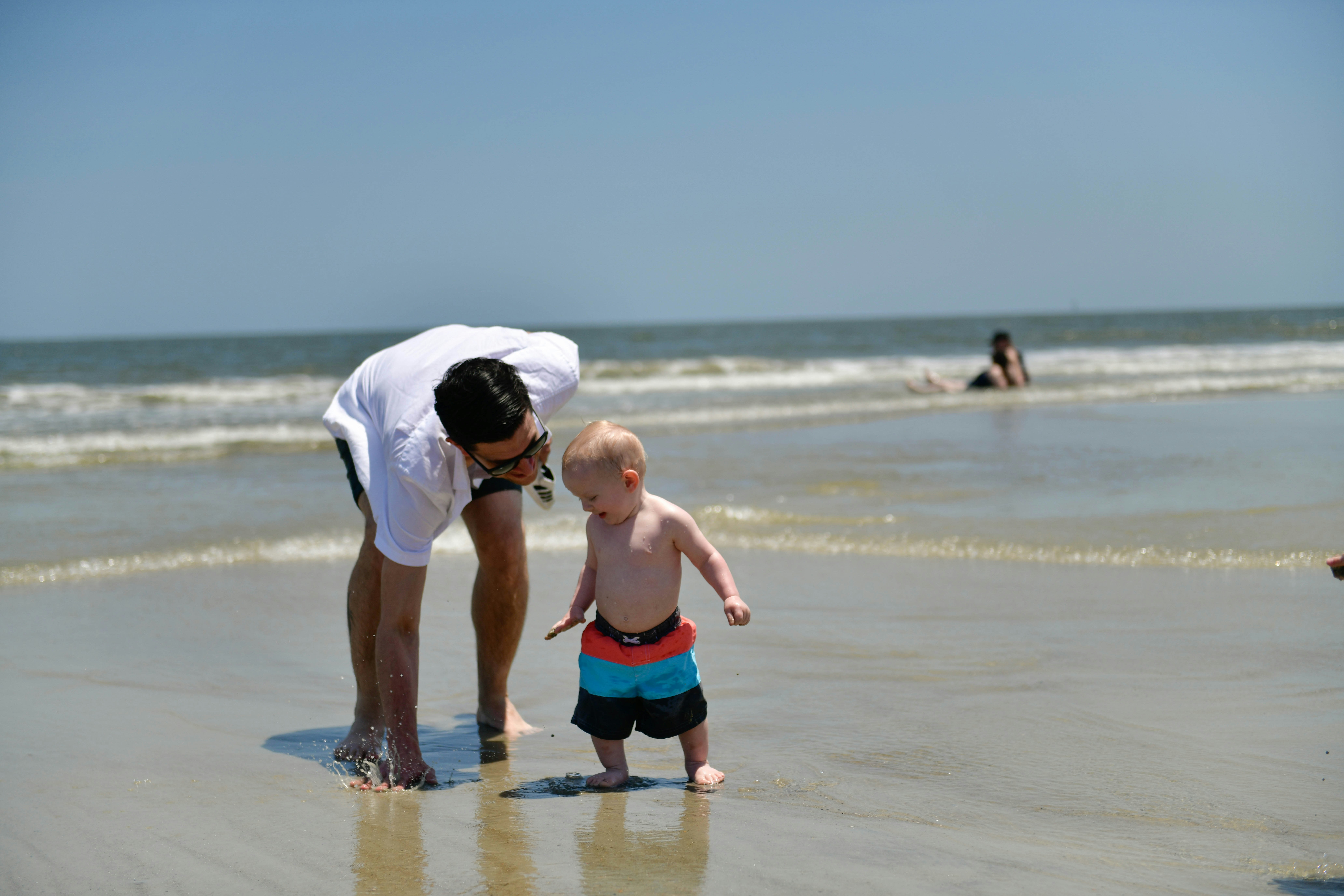 a man bending over to touch a small child on the beach, 