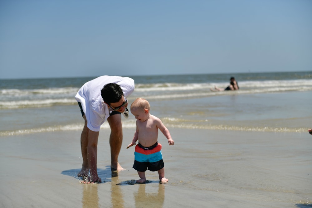 um homem se curvando para tocar uma criança pequena na praia