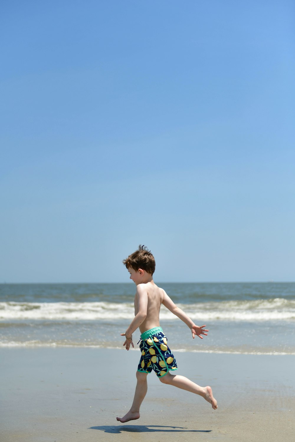 a young boy running on the beach with a frisbee