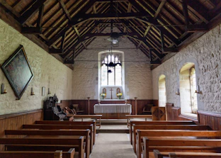 Interior of a small rustic chapel with wooden pews and soft natural light.