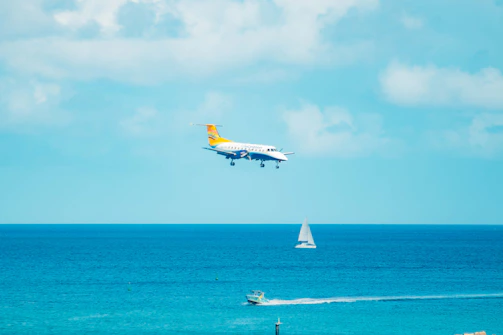 Bob piloting a helicopter above the sparkling ocean, with the catamaran visible below.