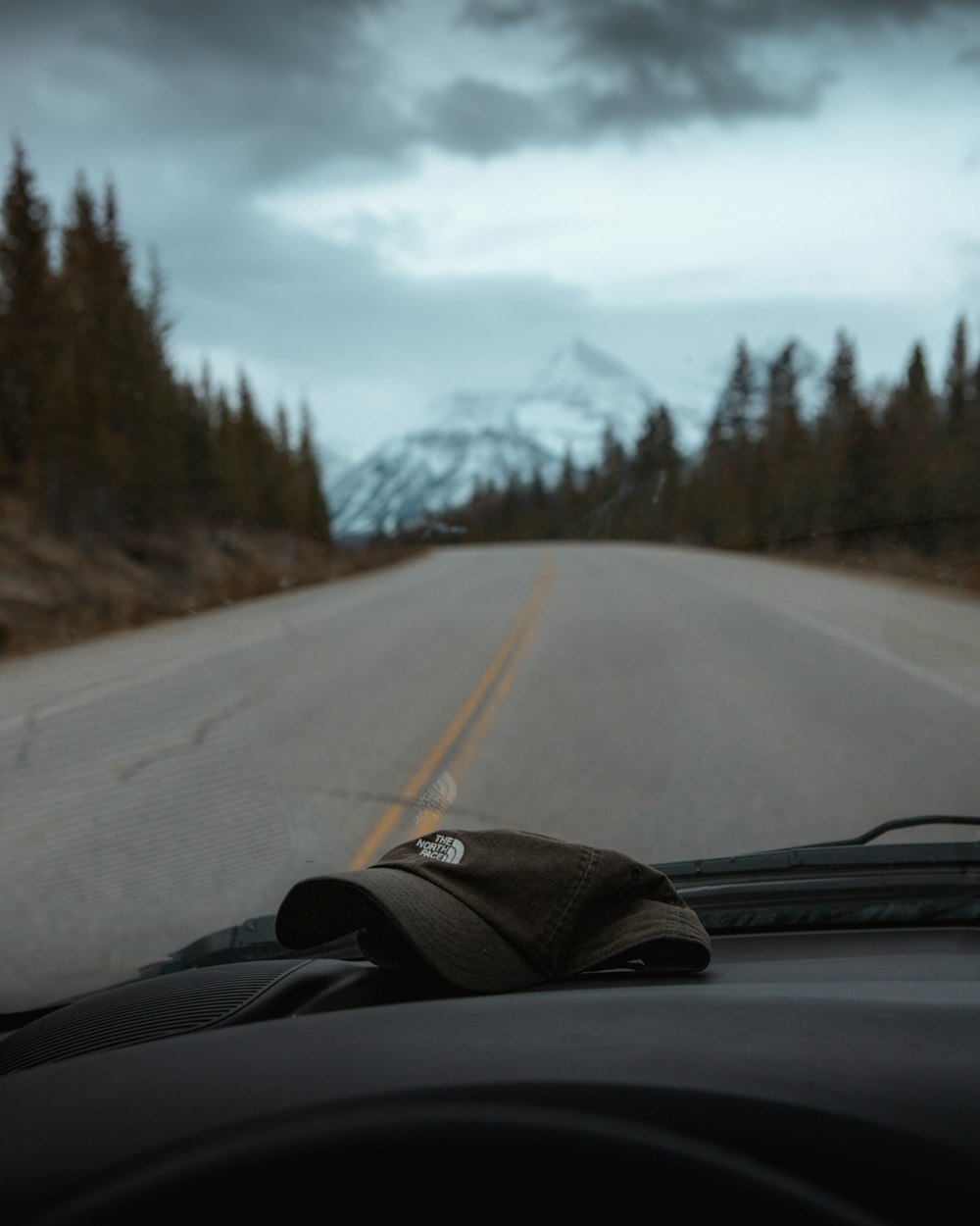a view from a car of a road with trees and mountains in the background