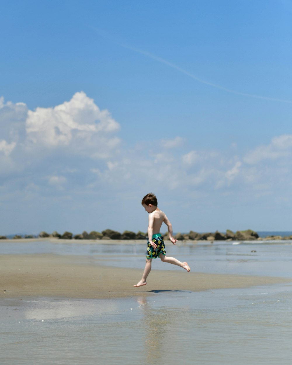 a young boy running on the beach with a frisbee