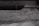 A textured concrete surface with visible roughness and small granules. The background is blurred, suggesting an industrial or urban setting.