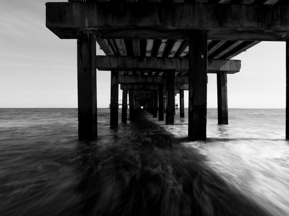 a black and white photo of the ocean under a pier