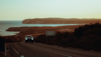 A winding coastal road in Italy with a vintage car driving along the cliffs at sunset.