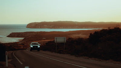 Dynamic shot of a car influencer driving along a scenic coastal highway at sunset.