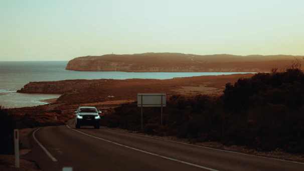 A winding coastal road with a vintage car driving under a golden sunset.