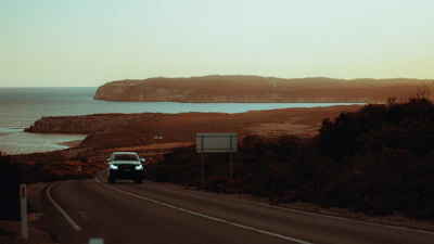 Dynamic shot of a car influencer driving along a scenic coastal highway at sunset.