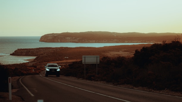 A scenic Moroccan coastal road with a tourist car driving along the shore at sunset.