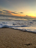 Gentle waves caressing a sandy shore under a pastel sunset sky.